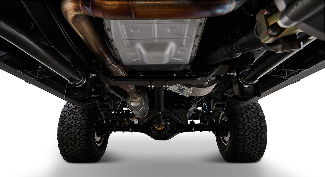 Undercarriage view showing exhaust system, rear axle, suspension, and tires of a Classic Ford Bronco