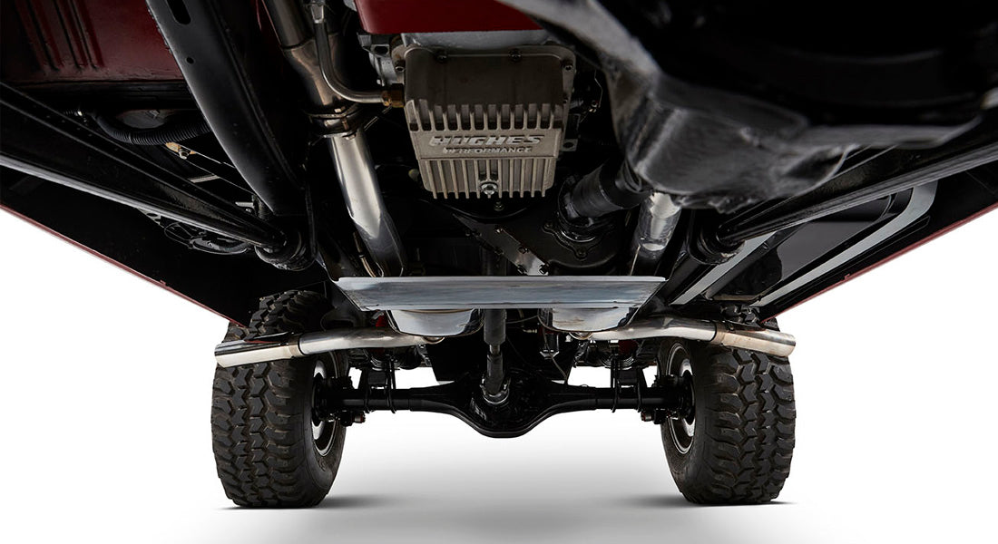 Undercarriage view showing dual exhaust system, suspension parts, and tires of a Classic Ford Bronco