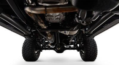 Undercarriage view of classic Ford Bronco showing suspension, exhaust pipes, and large tires