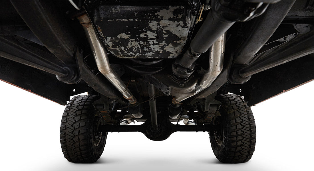Undercarriage view showing metal frame, axle, tires, and exhaust pipes of Classic Ford Bronco