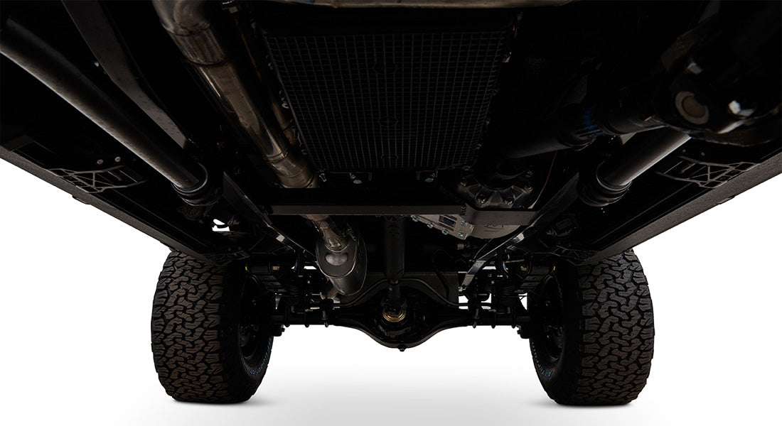Undercarriage view showing suspension, axle, exhaust, and tires against white background
